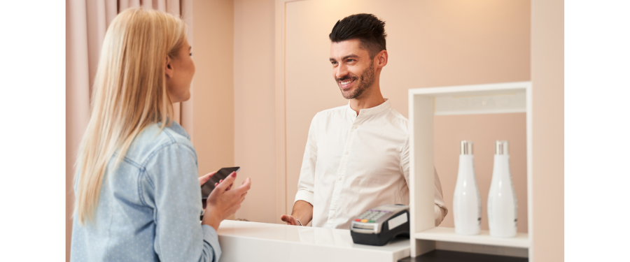 A woman checking out at a spa front desk with a male receptionist