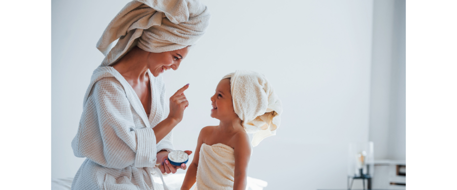 A mother and daughter in robes and towels playing with spa products and smiling at each other