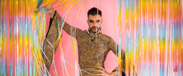 a man dressed up for bride standing in front of rainbow streamers